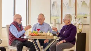 Older adults enjoying social activities at Sequoia Living. Two elderly men, one elderly woman. Holding drinks.