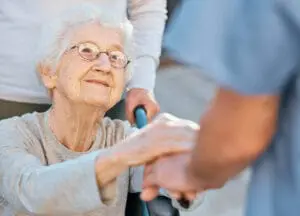 Holding hands, caregiver and senior woman in wheelchair for support outdoor in retirement home. Love, trust and healthcare nurse or medical wellness doctor for disability patient with kindness older woman, holding hand, skilled nursing