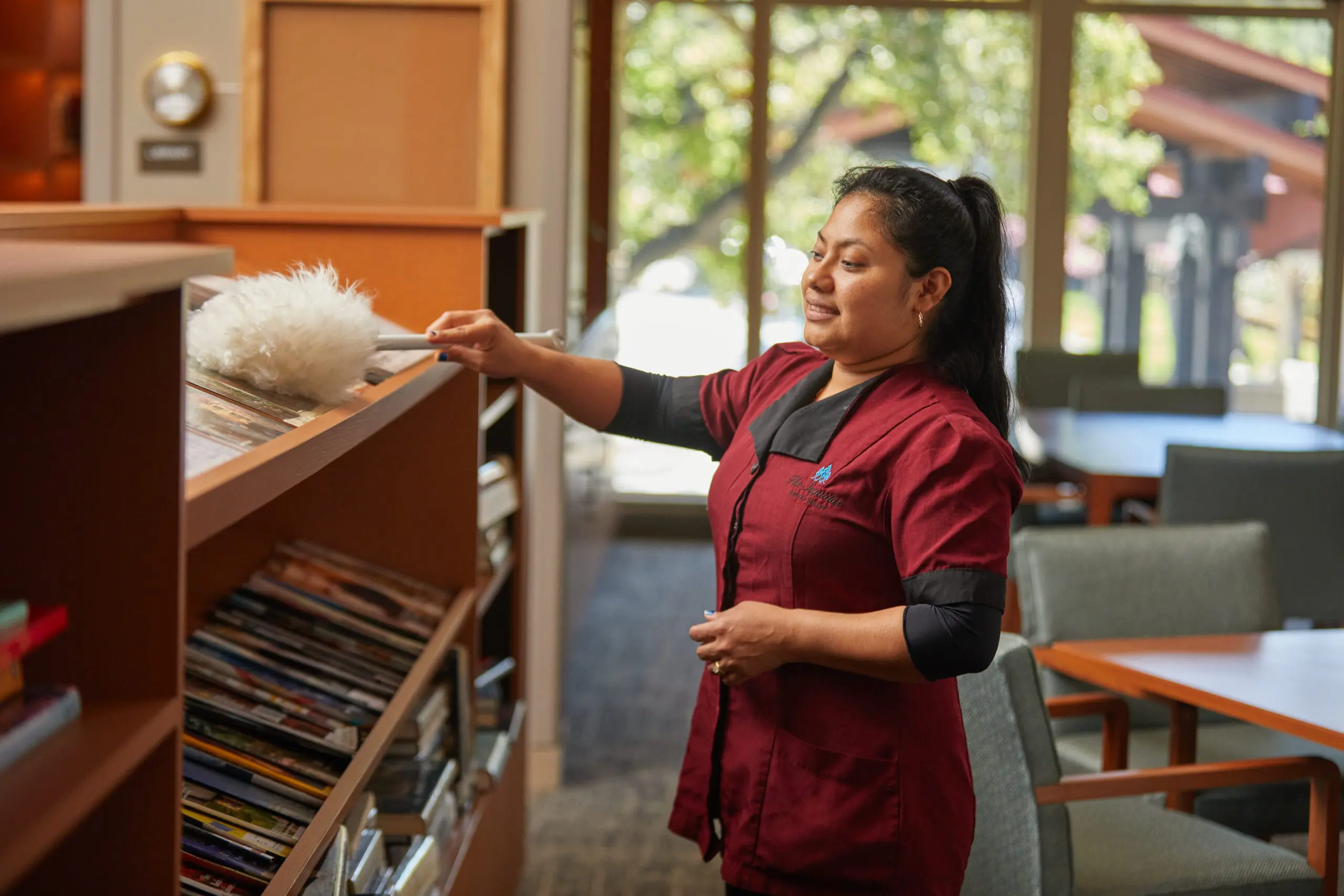 Young lady housekeeper dusting a shelf. Wearing a red top and red pants.