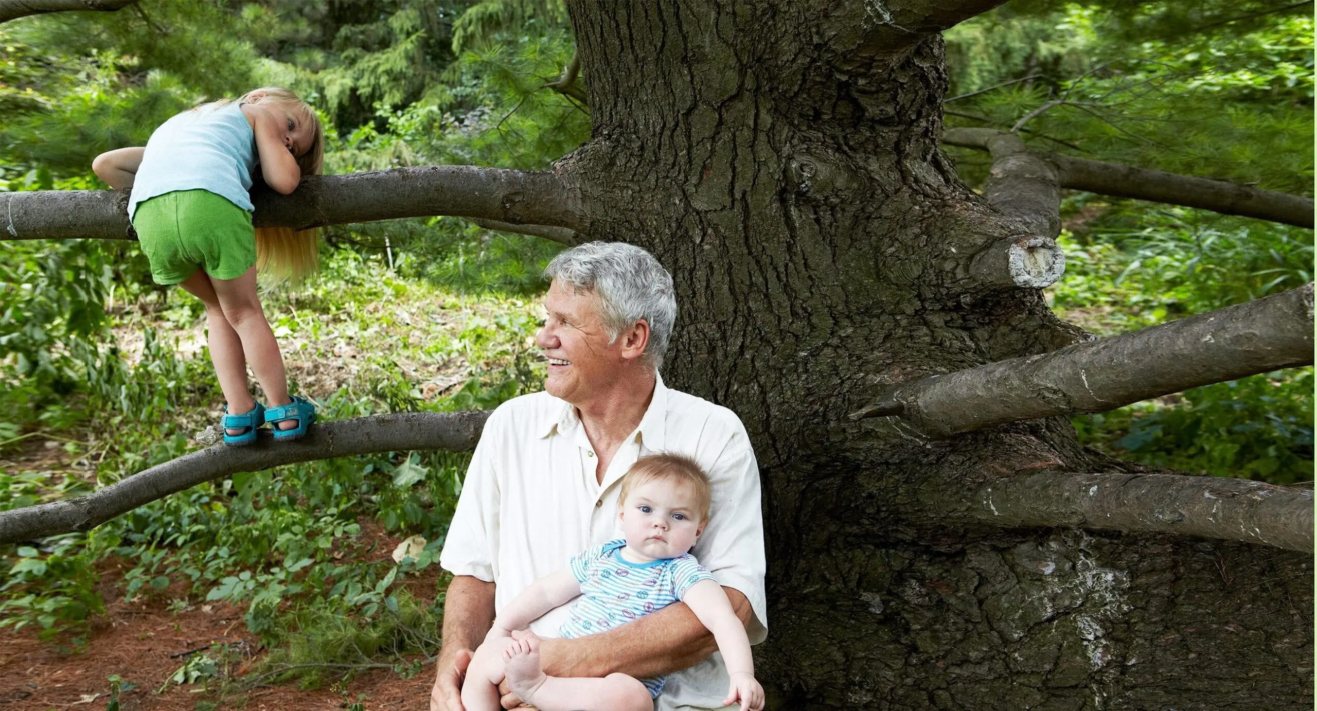 offset_comp_137906-e1647974654504 elderly man holding a baby while a child climbs a tree