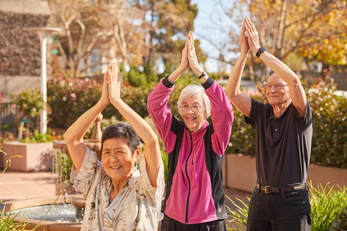 Health and Wellness at The Sequoias SF. Three elderly people doing yoga. One man, two women.