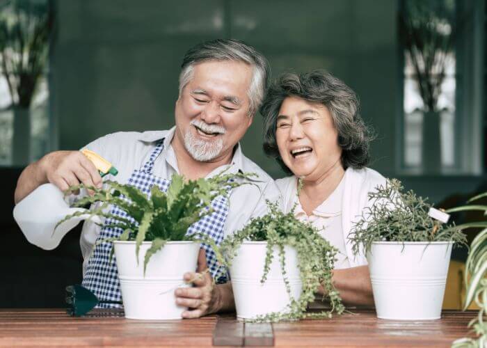 Elderly couple watering plants and laughing.