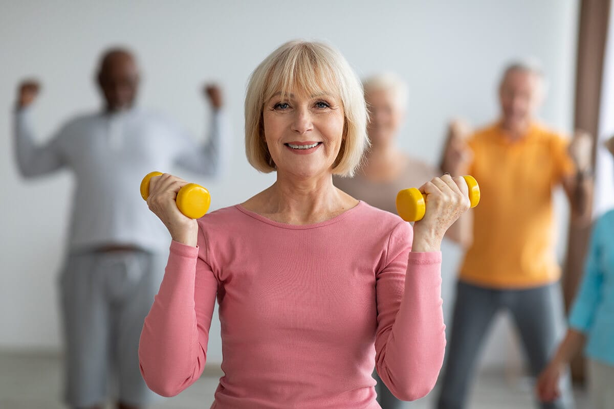 Movement. Older woman in main focus while working out, smiling.