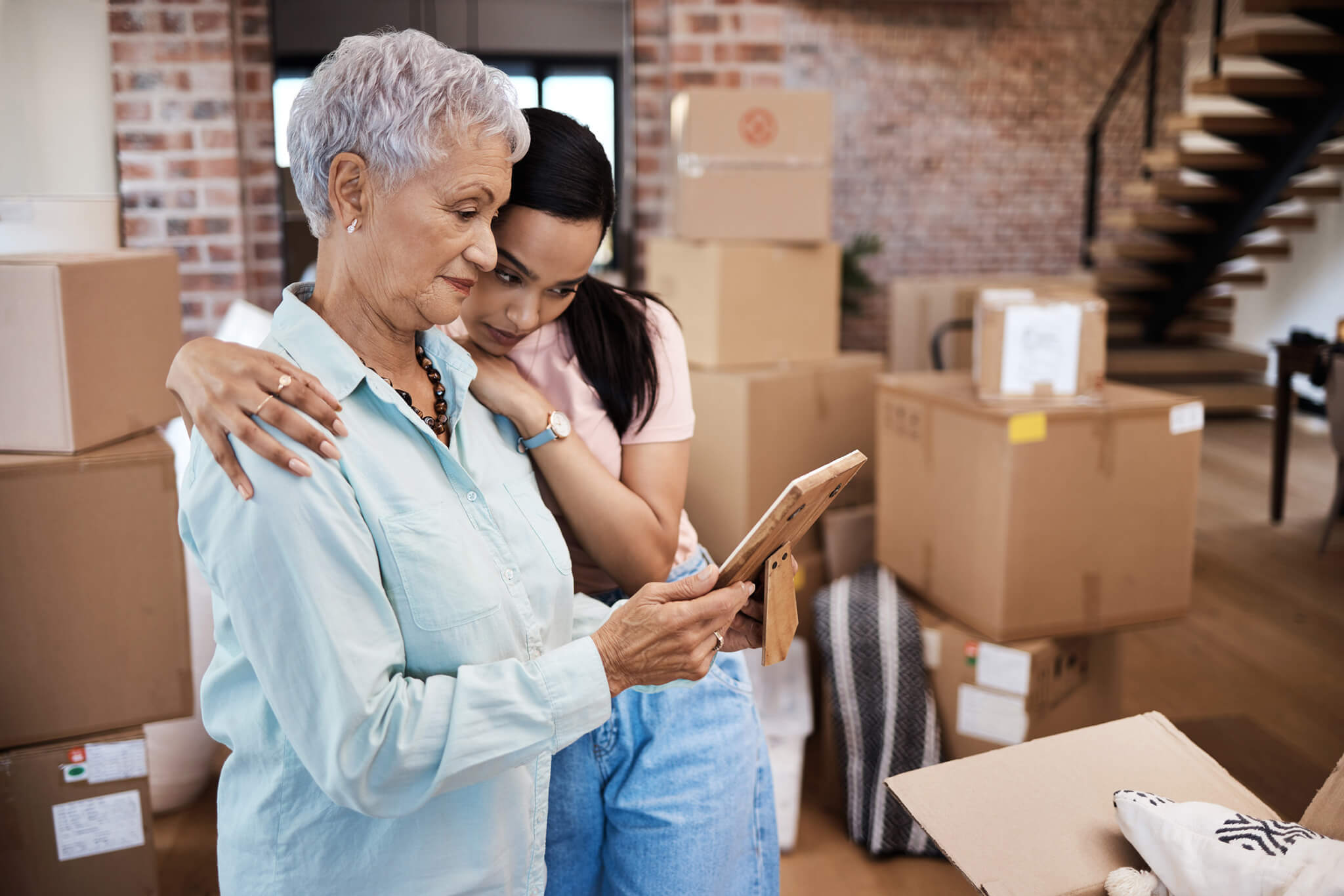 Downsizing article in SF Business Times. Olderwoman with younger woman resting head on shoulder with moving boxes in background.