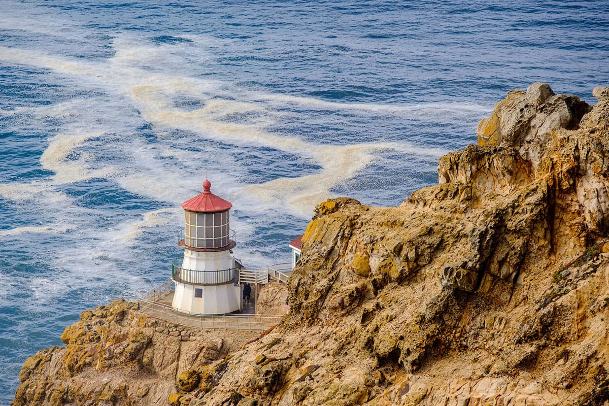 Hiking. Red and white lighthouse on cliff overlooking ocean.
