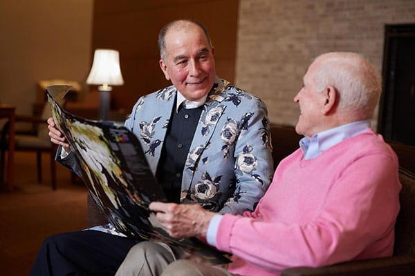 Two senior men sit on a sofa together looking at a photo album
