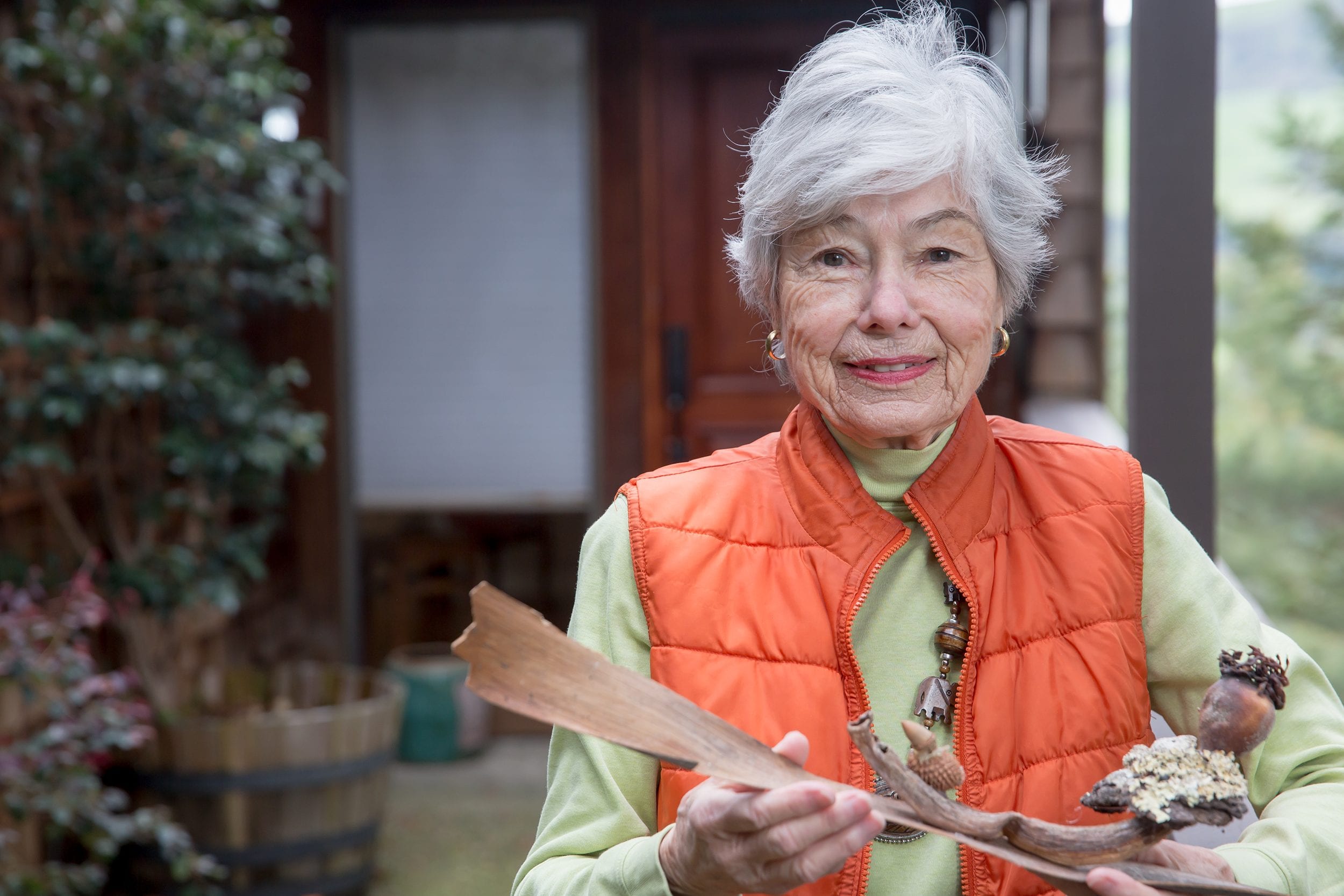 Elderly woman wearing orange vest holding tree bark and sticks