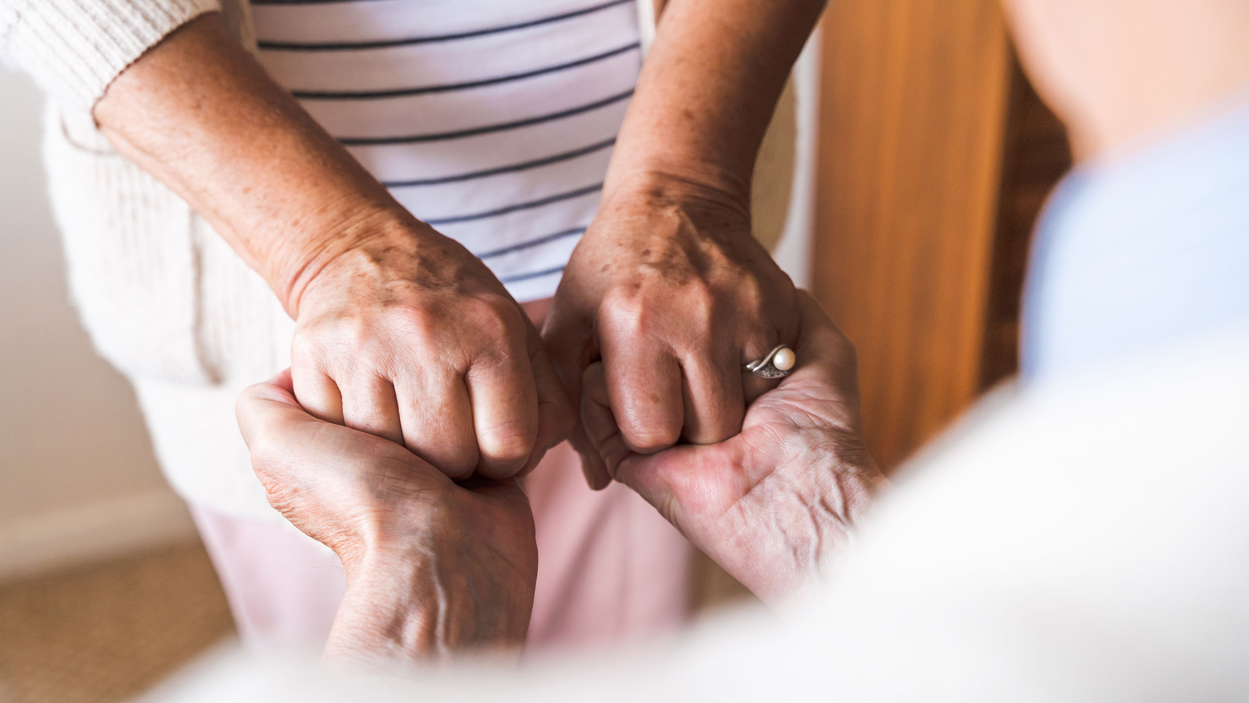 Close up of an older adult's hands clasping those of her caregiver
