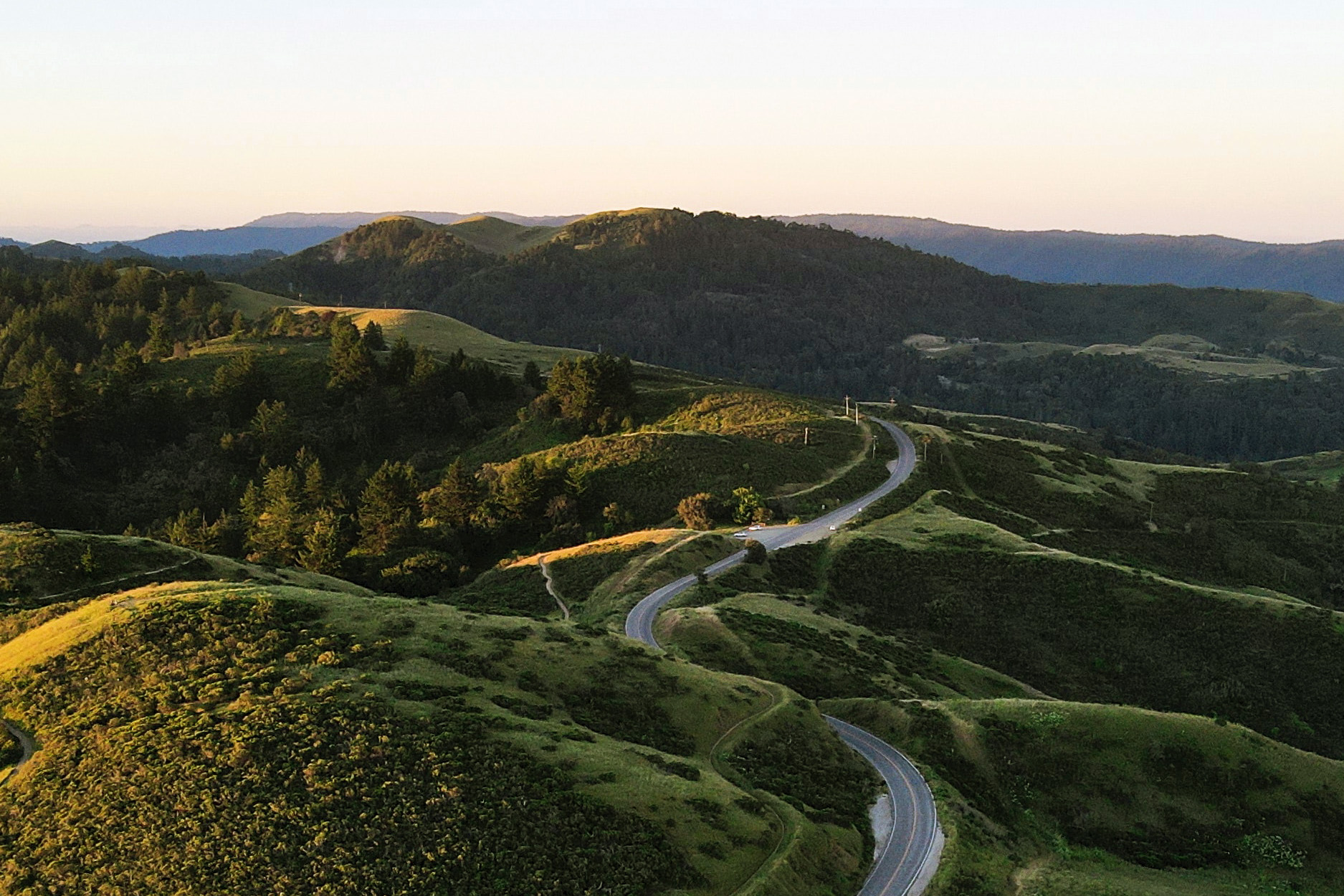 Arial image of Portola Valley at sunset. Rolling hills with one road winding through it.