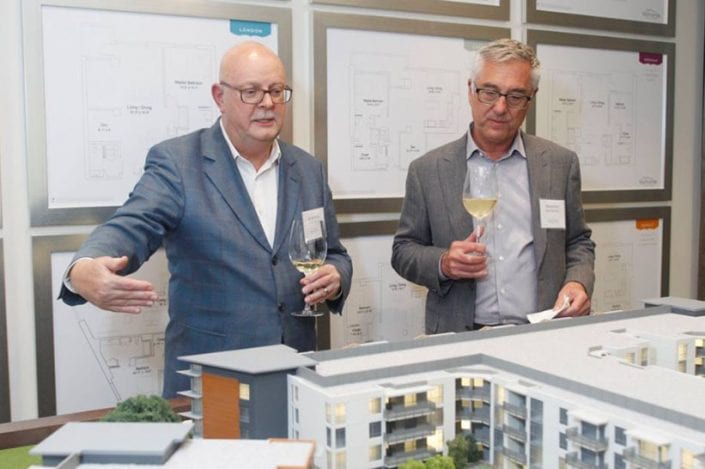 two men holding wine glasses talking about model of viamonte at walnut creek building