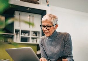 Elderly woman wearing glasses and sitting down using a laptop