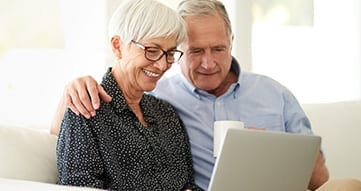 Elderly couple sitting on a couch while looking at laptop