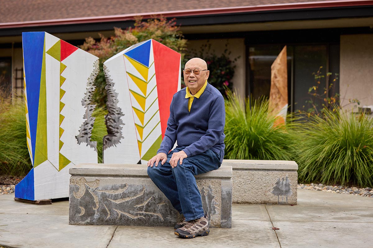 Older adult male, a resident, sits near his sculture