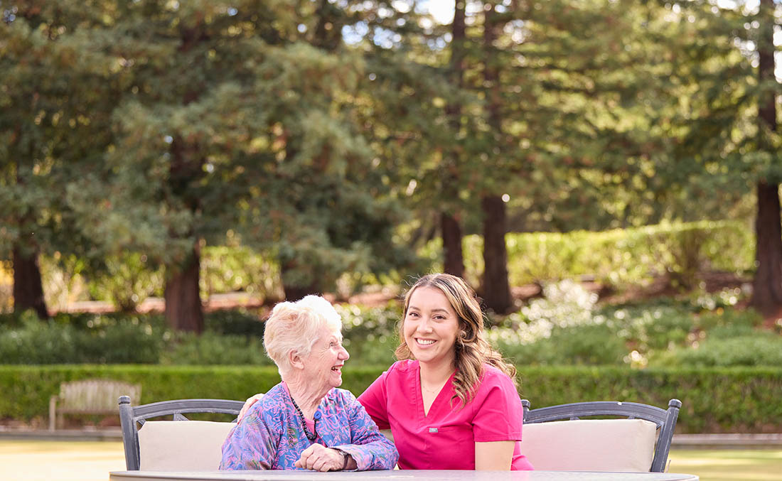 CareTaker Assisted Living vs Nursing Home, a happy female resident sitting outdoors with a nurse, caregiver