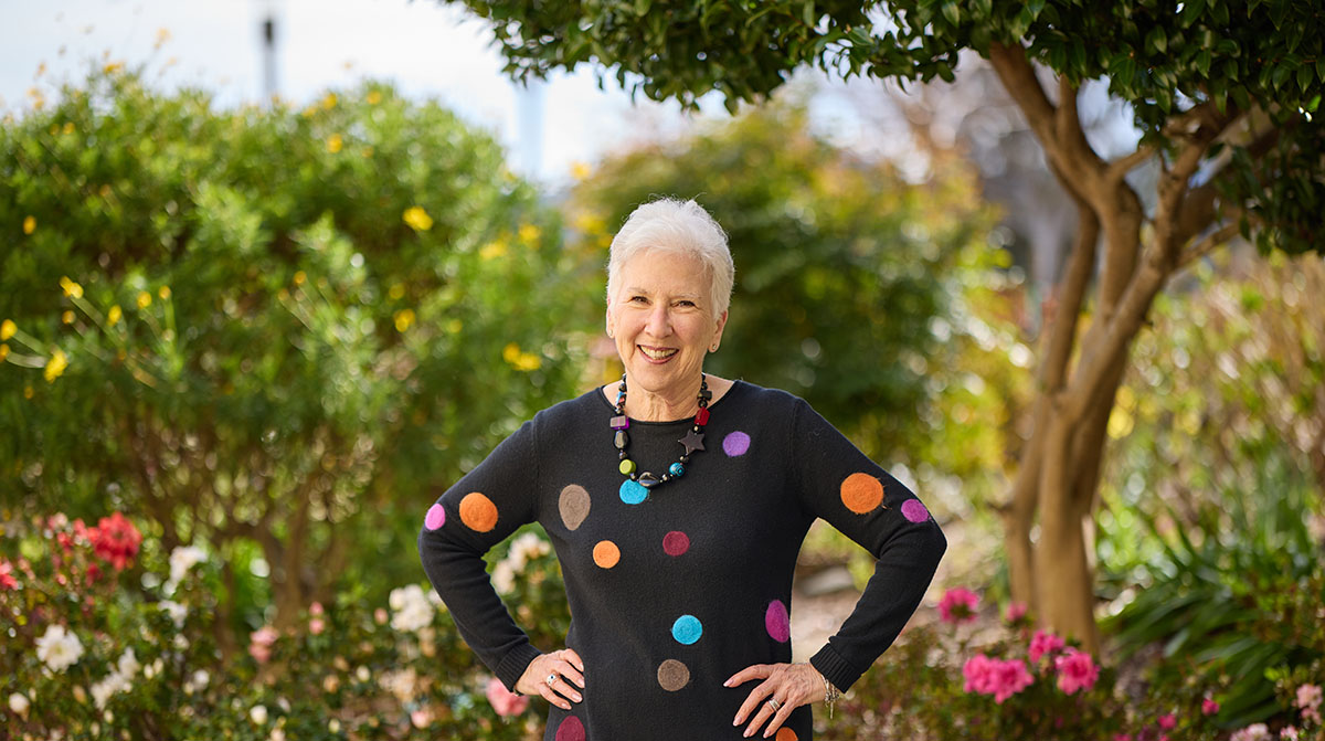 Ruth standing outdoors by garden, wearing a fun colorful top, Never Stop The Tamalpais Marin Sequoia Living